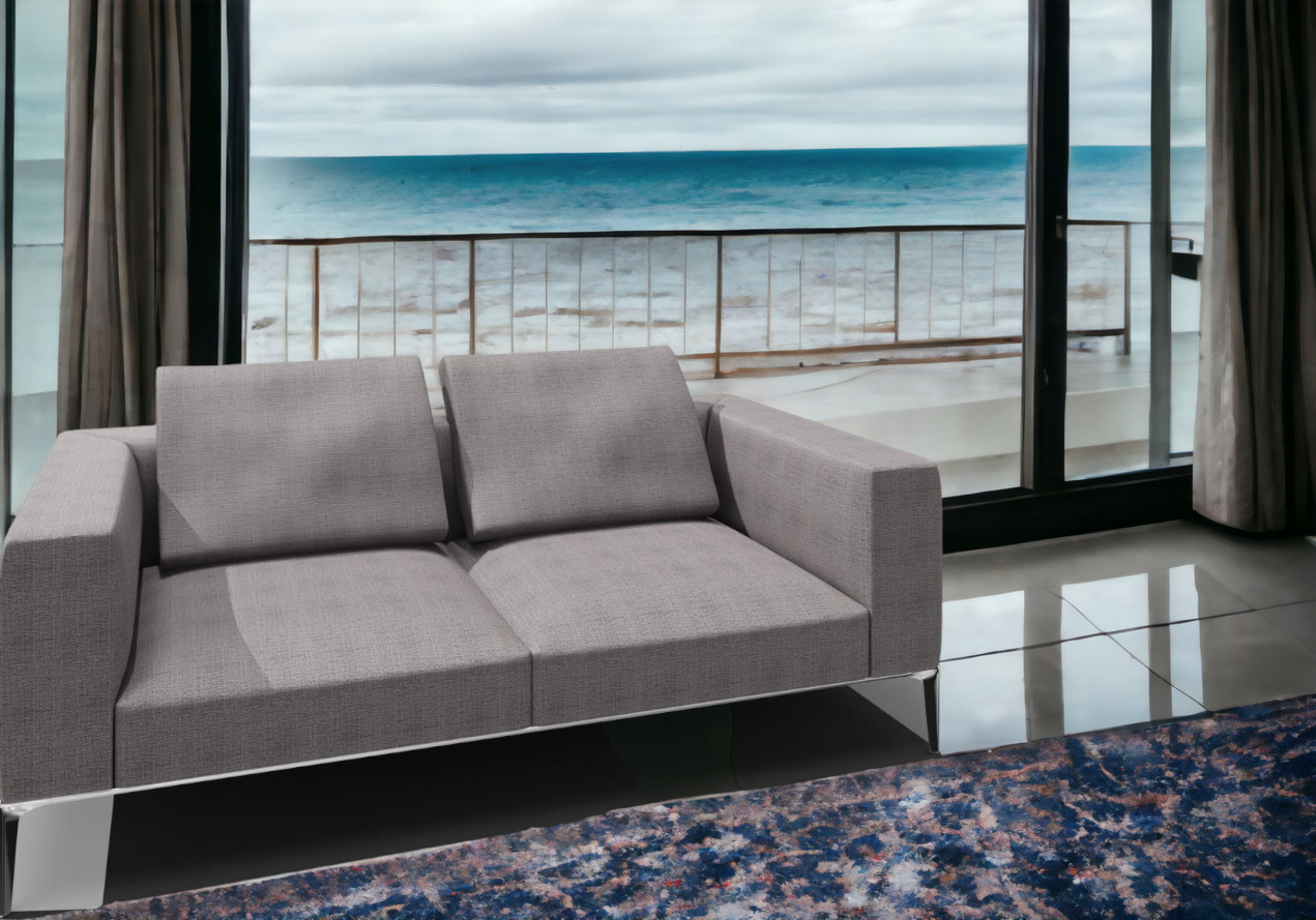 Jaan Living Sofa, 2,5 Sitzer in Grau mit zwei Rückenkissen vor Fenster mit Meerblick.