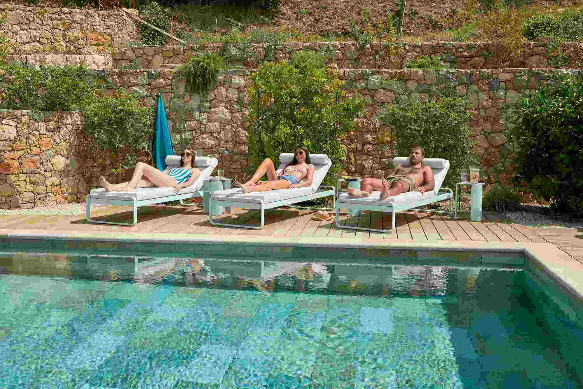 Drei Personen entspannen auf modernen Bellevie Sonnenliegen am Pool; Outdoor-Möbel für Garten und Terrasse.