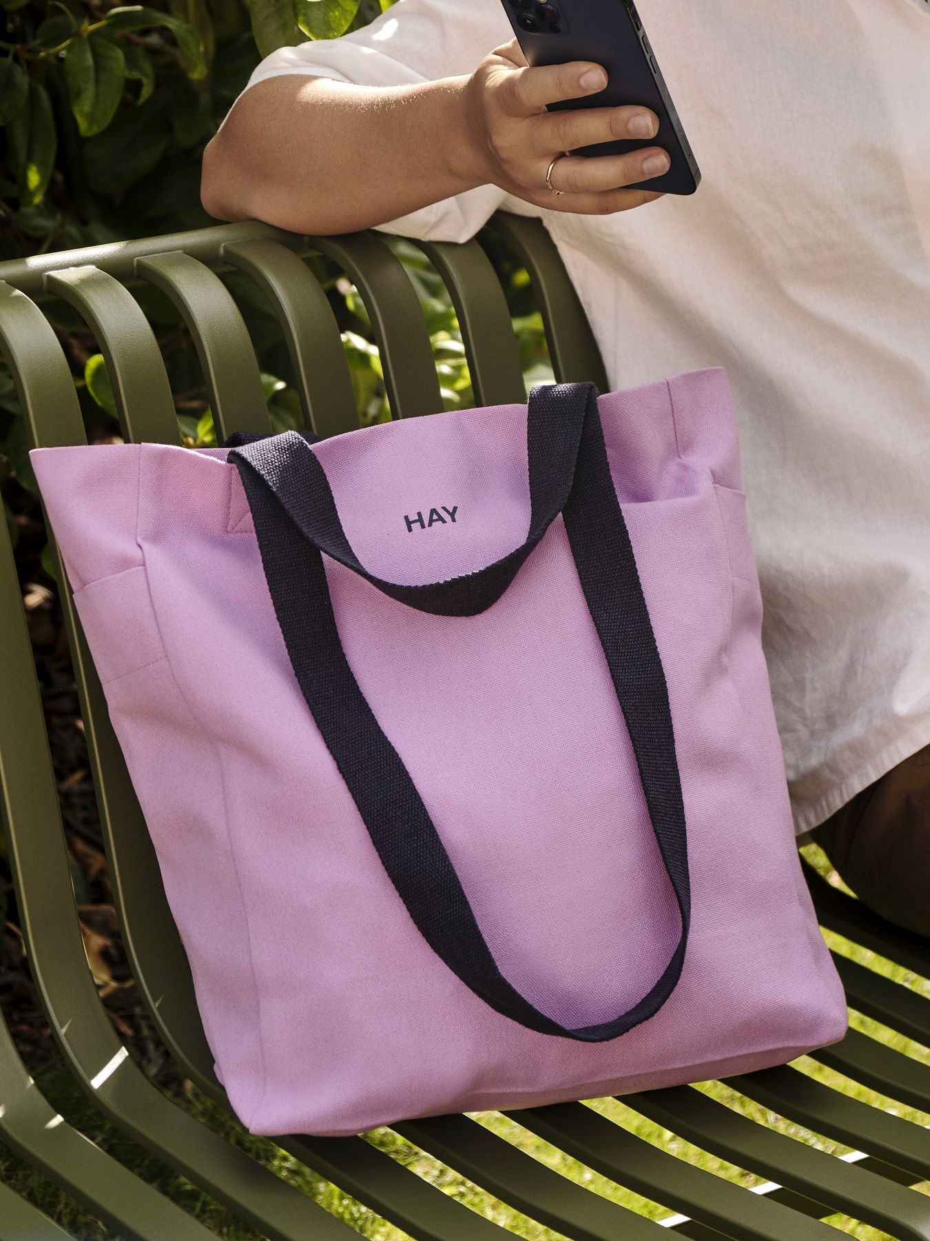 Nahaufnahme einer rosa Hay Everyday Tote Bag Tasche mit schwarzen Trägern auf einer Parkbank.