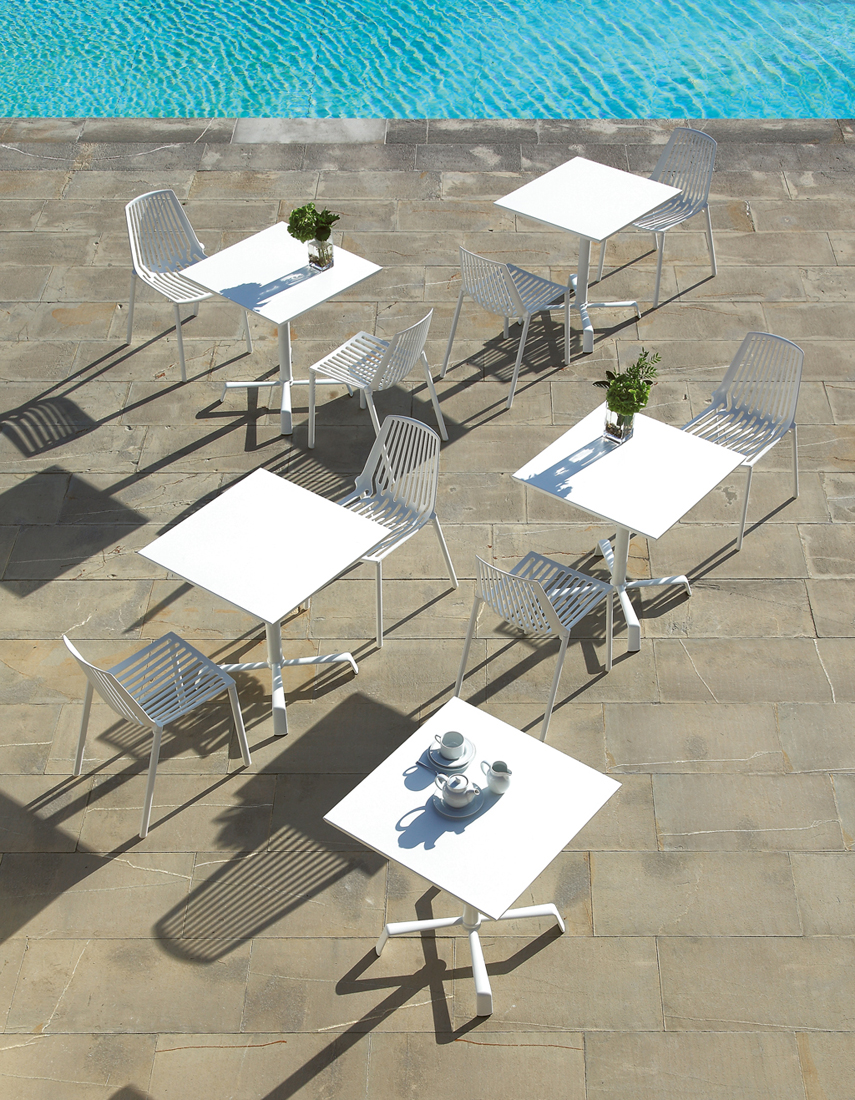 Mehrere weiße Rion Outdoor Stühle und Tische auf einer Terrasse neben einem Pool. Gartenmöbel-Set.