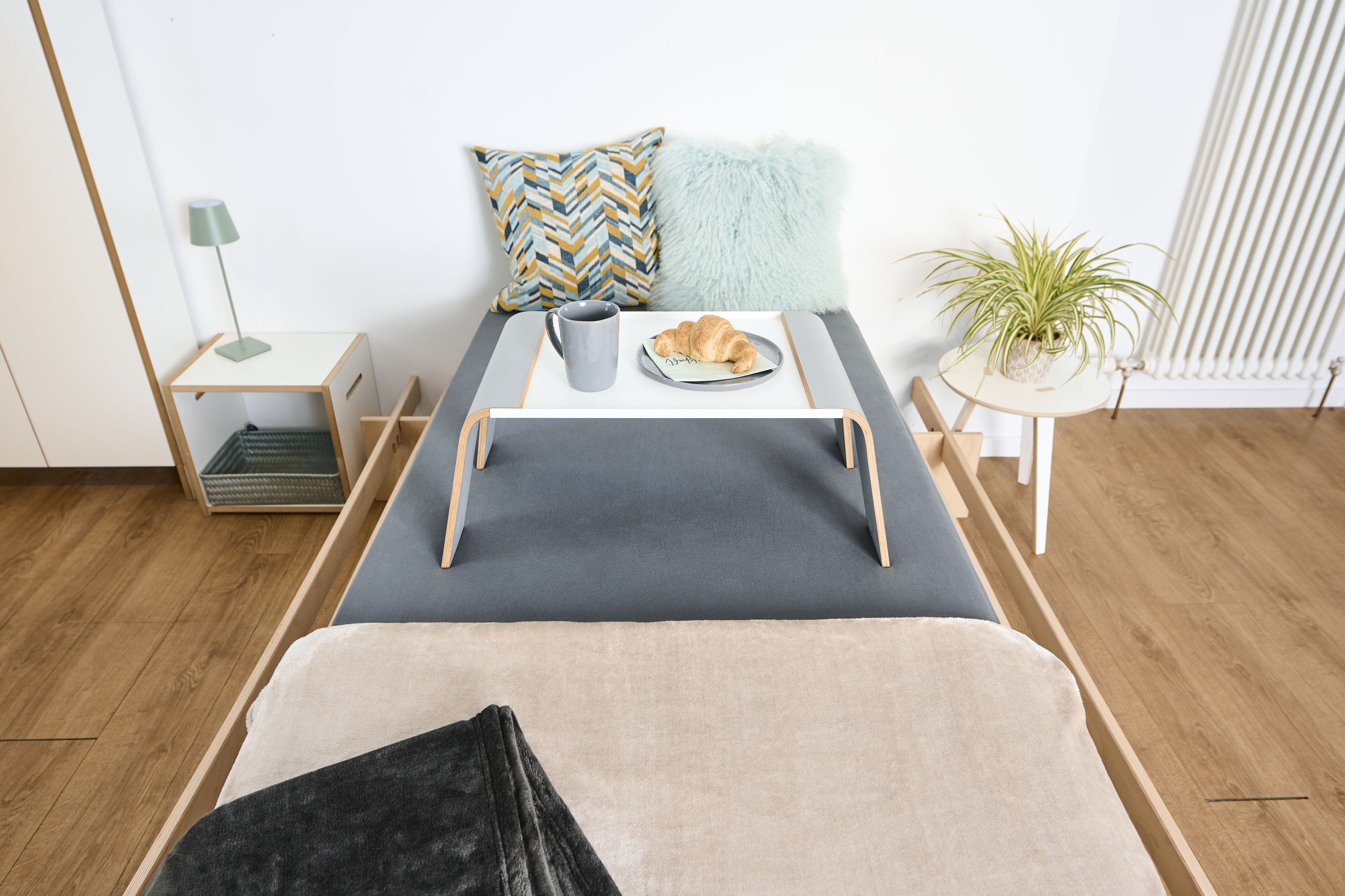 Tojo Notebook-Tablett als Frühstückstablett im Bett mit Croissant und Kaffee für entspanntes Aufwachen.