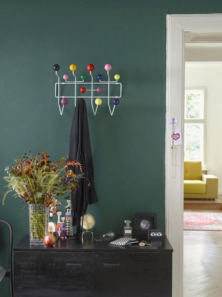 Bunte Garderobe mit Kugeln und Jacke an grüner Wand über schwarzer Kommode im Flur.