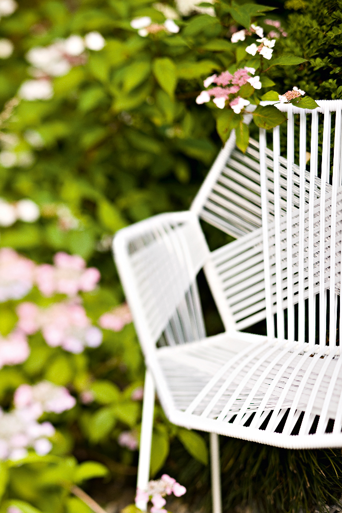 Detailaufnahme des weißen Tropicalia Armchair Outdoor Armlehnenstuhls von Moroso im Garten mit Blumen.