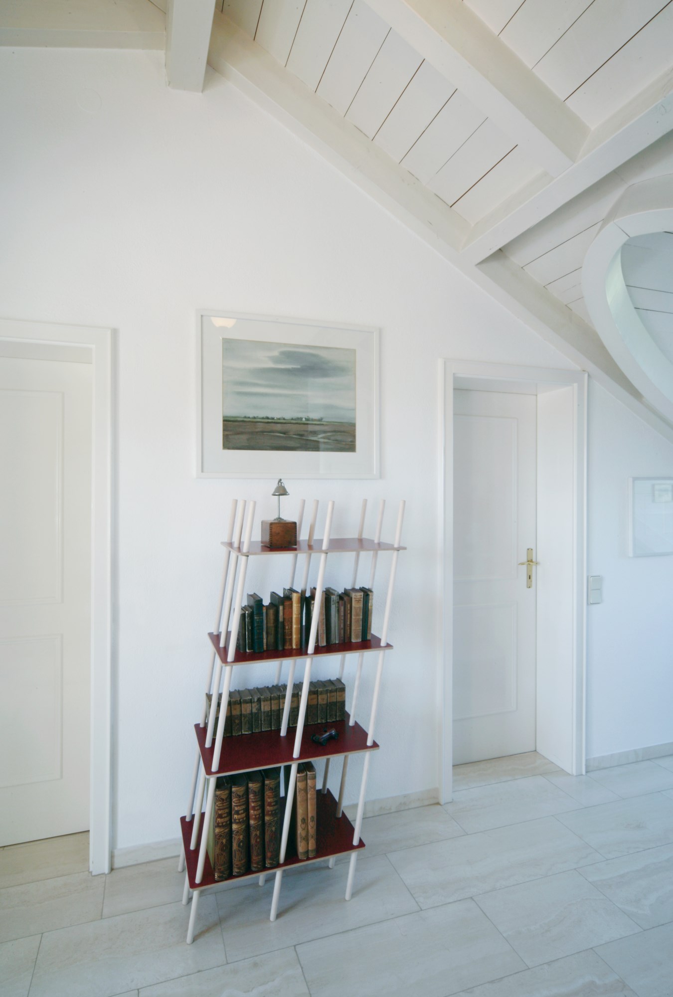 Nils Holger Moormann Regal mit Büchern in einem hellen Raum mit Dachschräge und weißen Wänden.