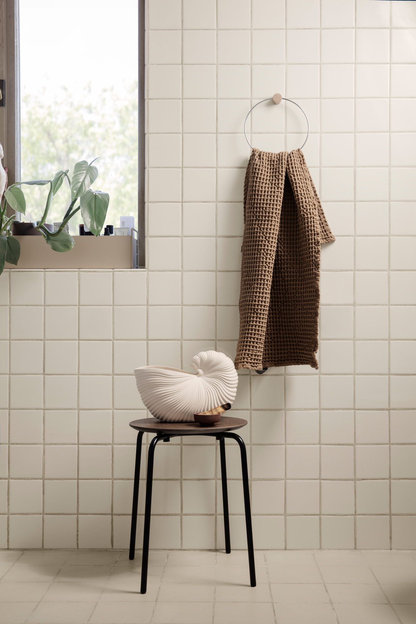 Helle Badezimmer-Szene mit Ferm Living Shell Pot Vase auf Hocker, Handtuch an der Wand.