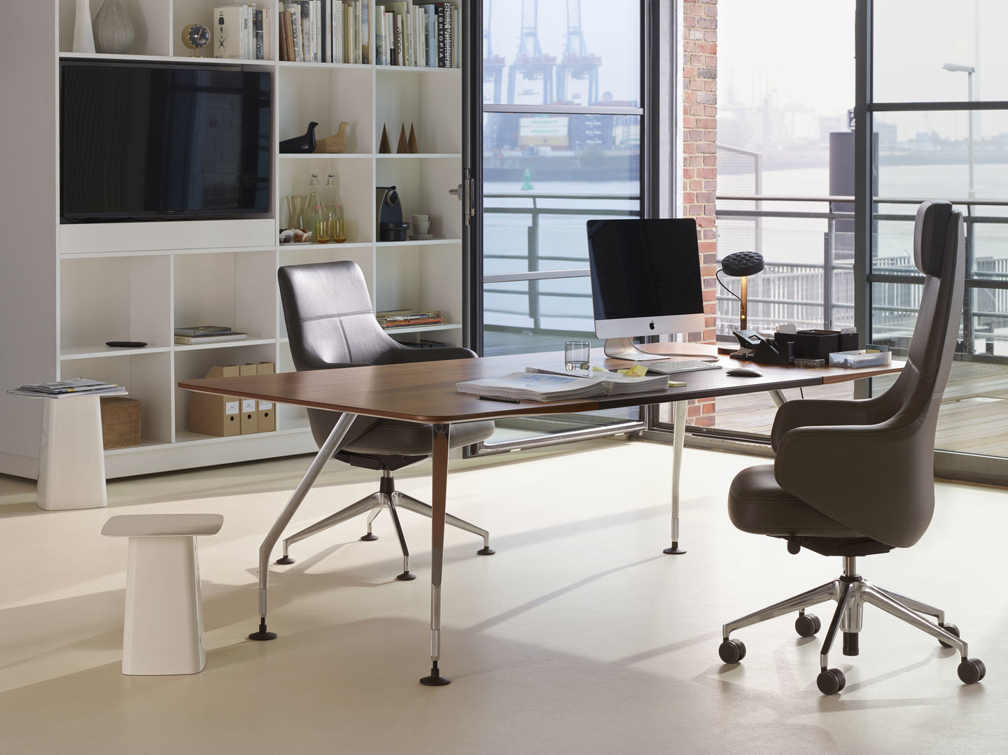 Büro mit Vitra Grand Executive Highback Konferenzstuhl aus Leder, Schreibtisch und Regalen vor Fenster.