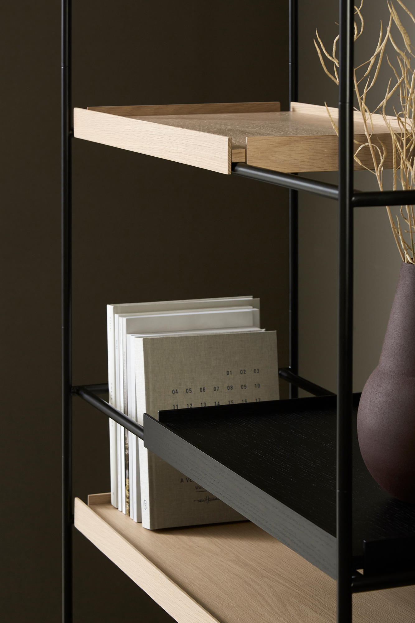 Detailaufnahme des hohen Tray Regals von Woud, Eiche natur und schwarz, mit Büchern und Dekoration.