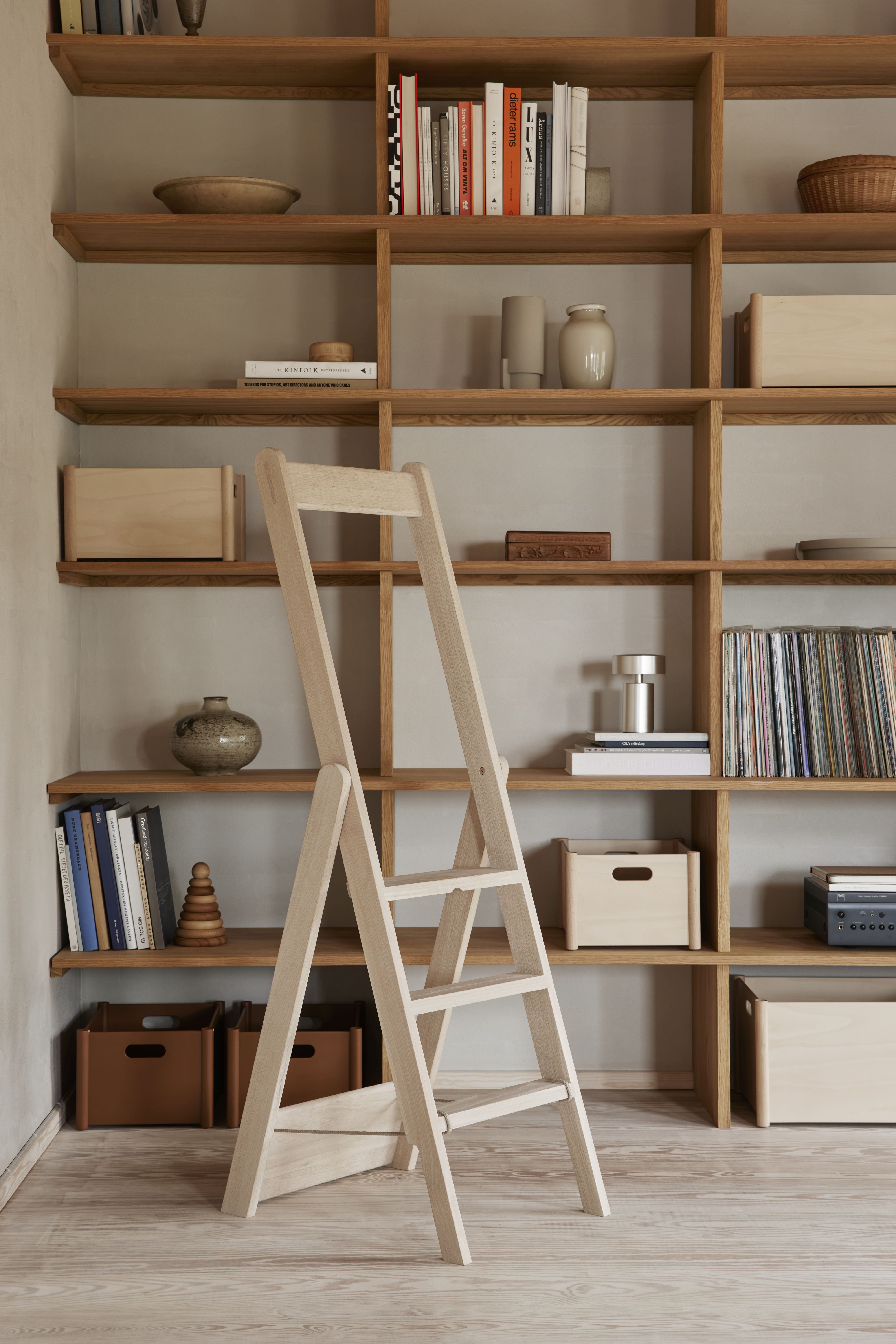 Step By Step Leiter aus hellem Holz vor einem vollen Bücherregal mit Holzregalen.