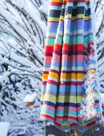 Weishäupl Klassiker Schirm: Detailaufnahme eines geschlossenen, farbenfrohen Sonnenschirms im Winter, teilweise mit Schnee bedeckt.