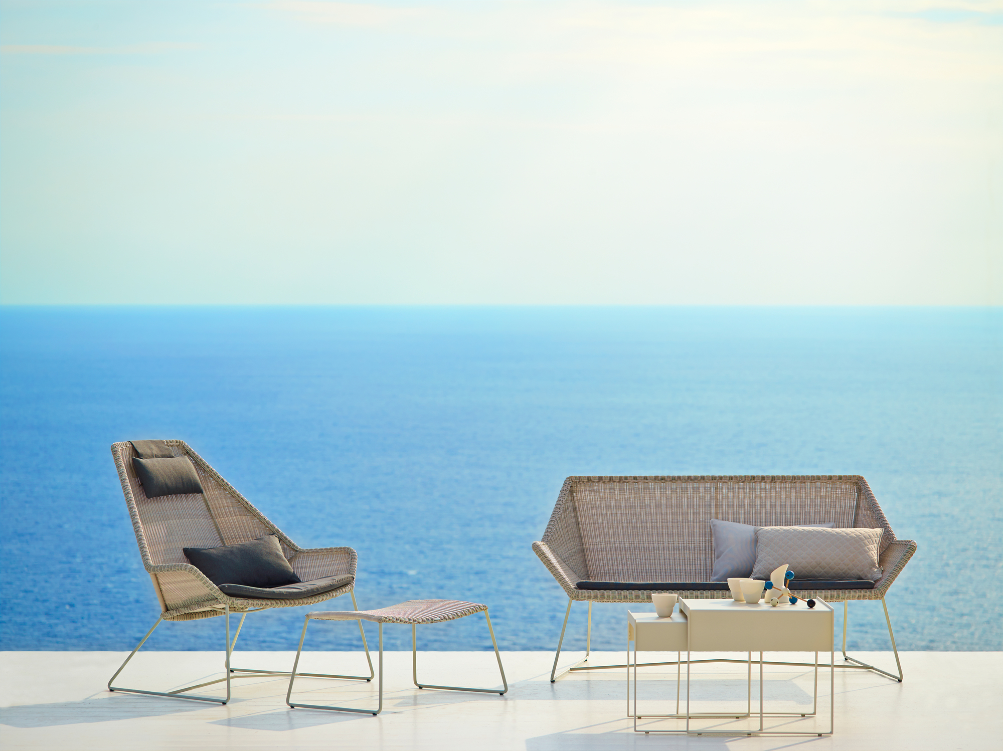Cane-Line Breeze Outdoor Hocker in Schwarz, Teil eines Loungesets mit Meerblick.