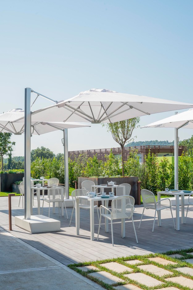 Quadratische, weiße Outdoor-Tische von Emu Nova mit Stühlen unter Sonnenschirmen auf einer Terrasse.