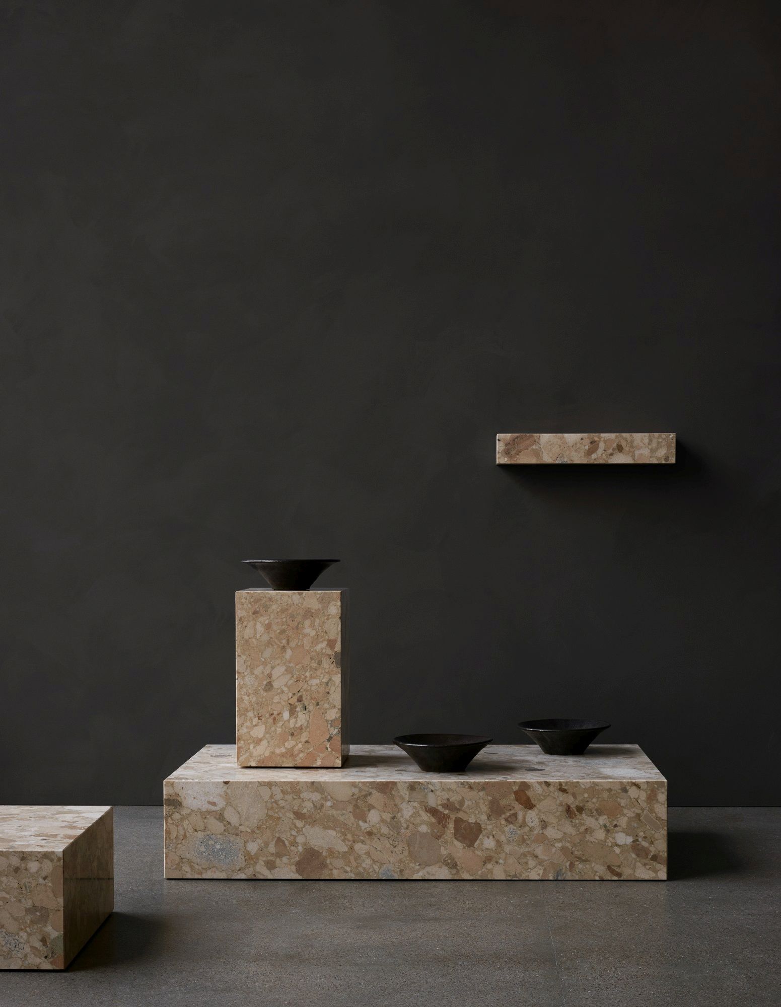 Audo Copenhagen Plinth Shelf Regal aus Marmor mit schwarzen Schalen vor dunklem Hintergrund.