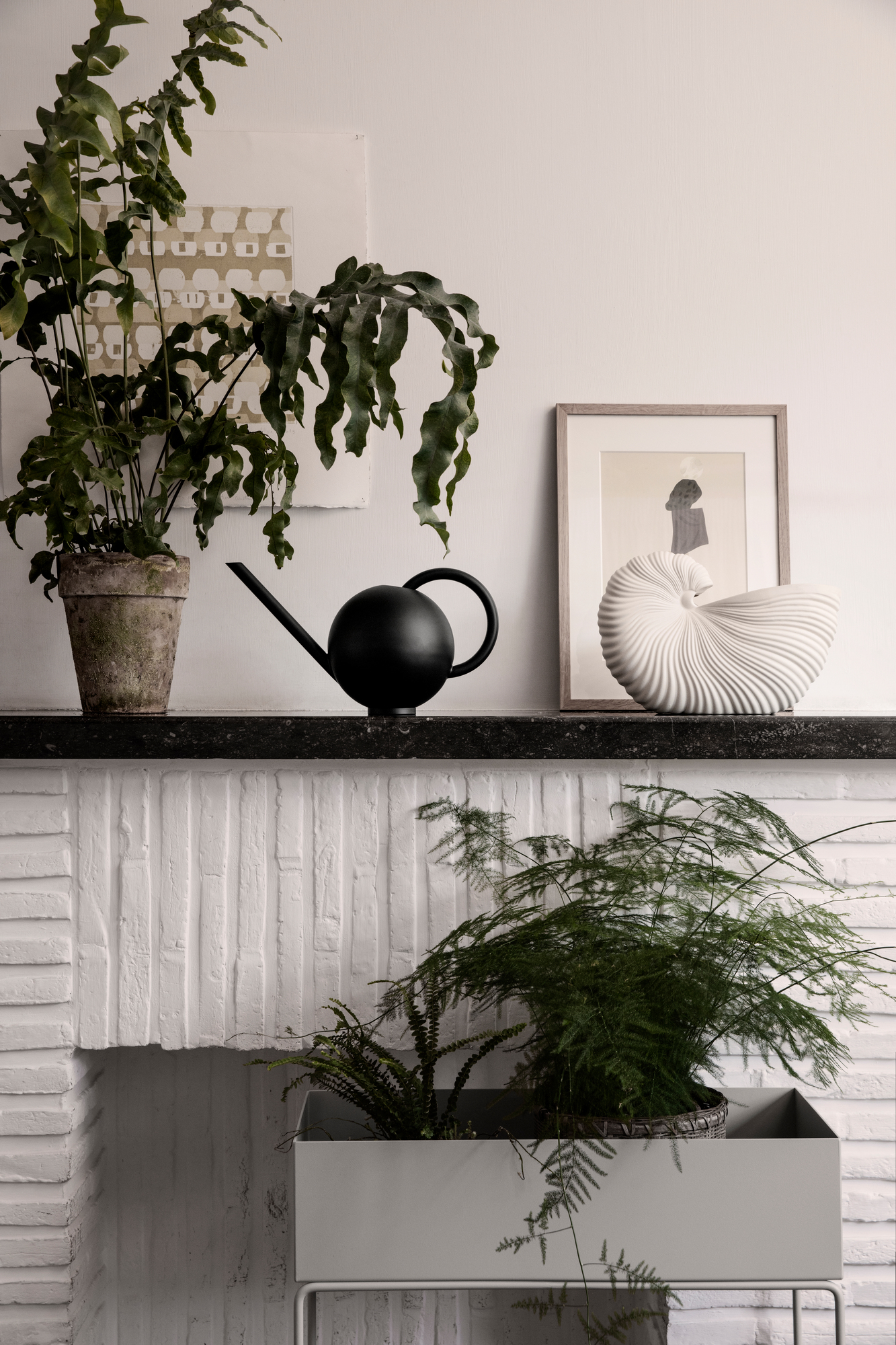 Nahaufnahme der Ferm Living Shell Pot Vase, einer dekorativen Keramikvase in Muschelform, auf einem Kaminsims mit Pflanzen.