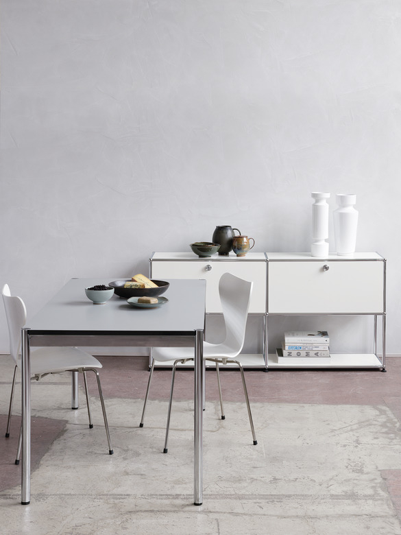 USM Haller Tisch 150x75 cm in Hellgrau mit Chromgestell und passendem weißen Sideboard im Hintergrund.