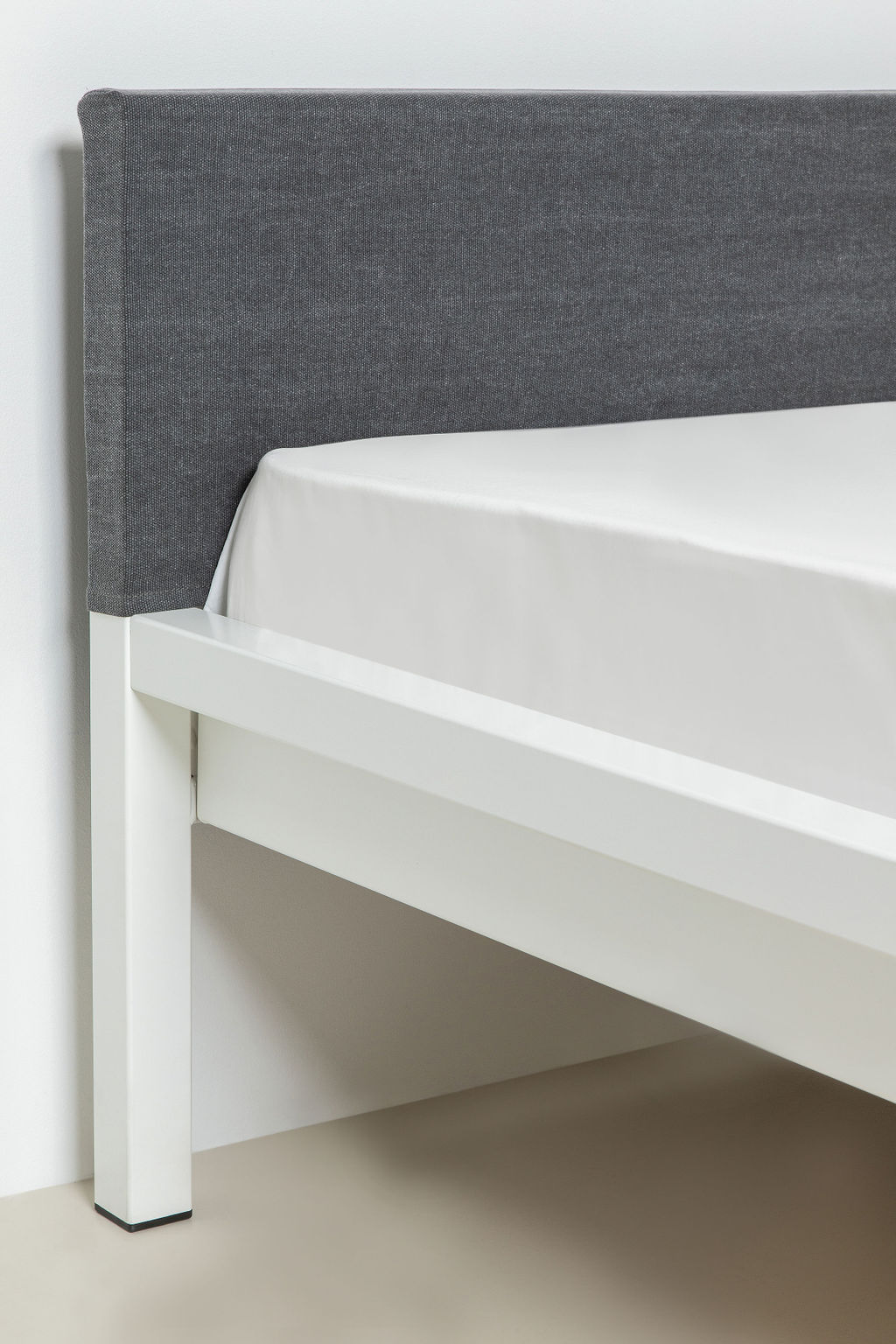 Nahaufnahme: Grauer Kopfteil Bezug für Hans Hansen Pure Bett mit weißem, pulverbeschichtetem Stahlrahmen.