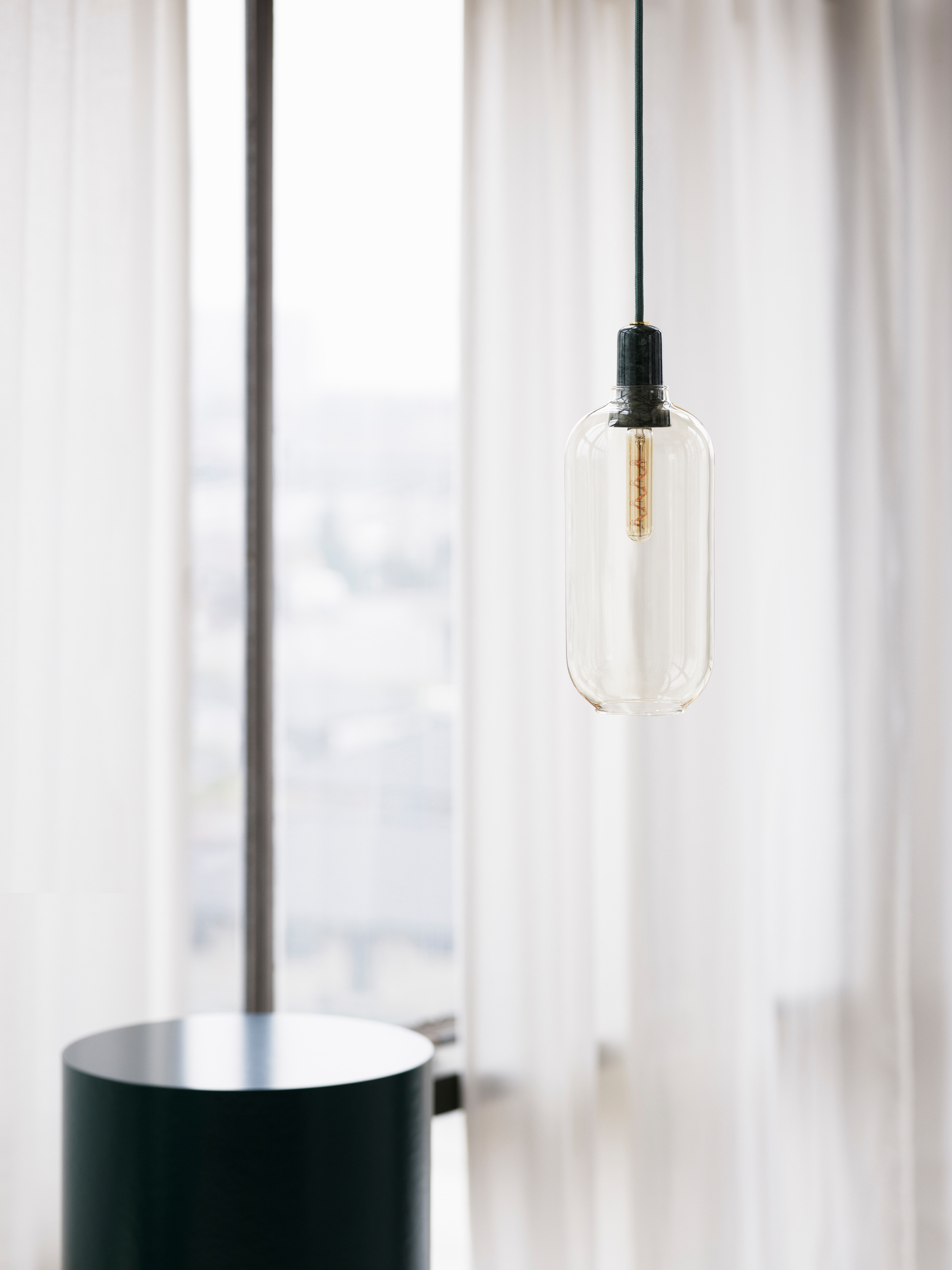 Nahaufnahme der Normann Copenhagen Amp Hängeleuchte mit klarem Glasschirm.