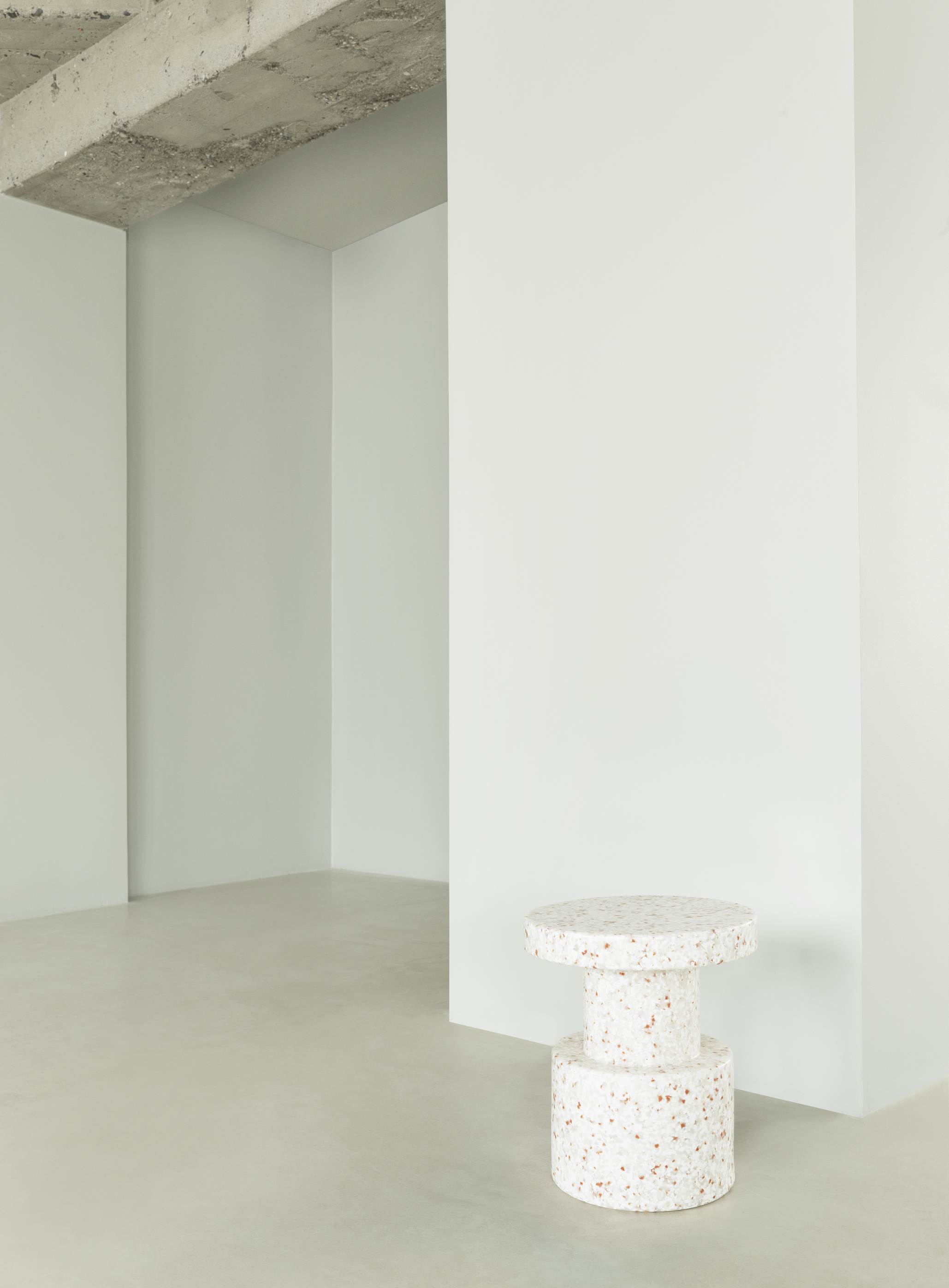 Normann Copenhagen Bit Stool Hocker in Weiß mit Terrazzo-Muster vor minimalistischem Hintergrund.