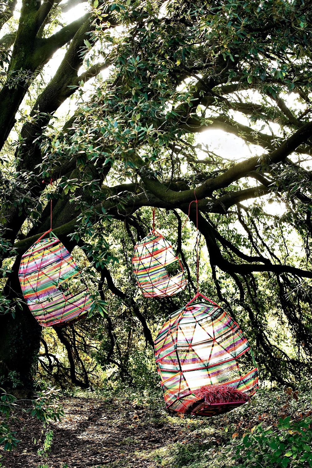 Drei bunte Hängesessel im Boho-Stil hängen an einem Baum im Garten, Outdoor-Möbel.