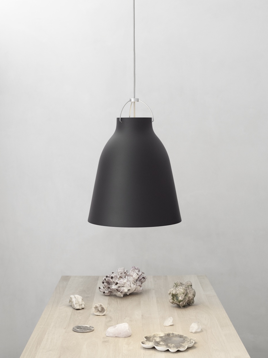 Schwarze Caravaggio Pendelleuchte von Fritz Hansen über einem Tisch mit Dekosteinen und Muscheln.