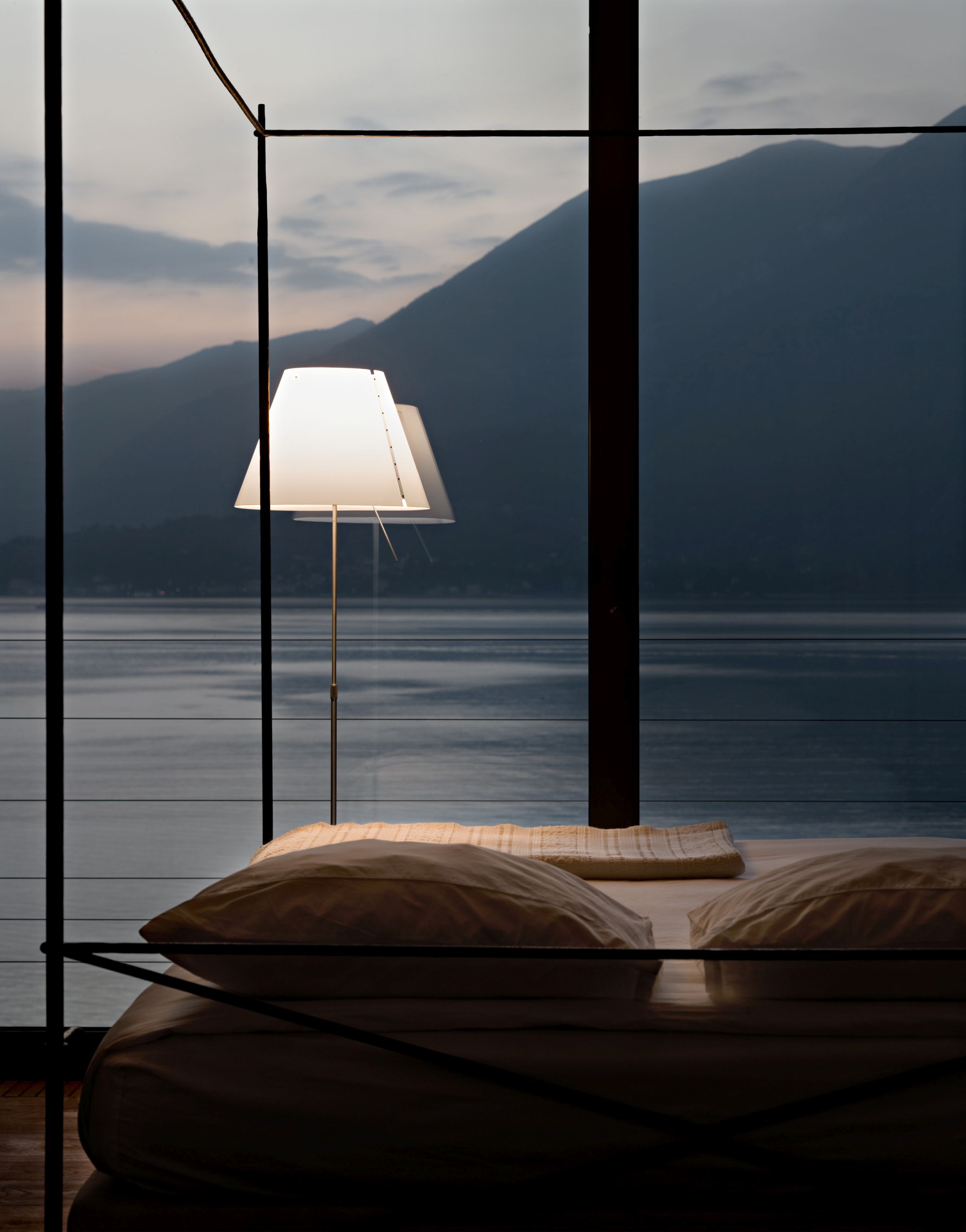 D13 Costanza Tischleuchte von Luceplan neben einem Bett mit Seeblick.
