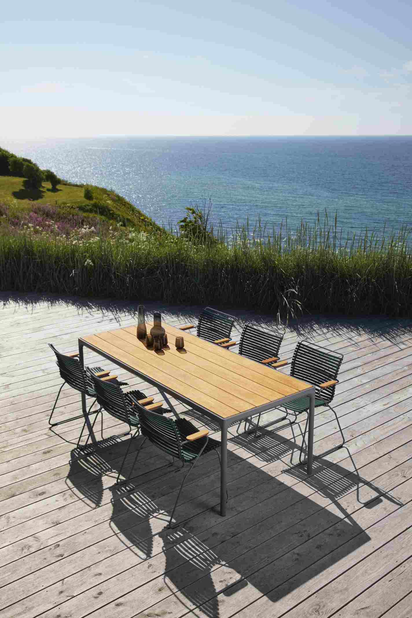 Dunkelgraue Click Dining Stühle mit Armlehne von Houe und Esstisch auf Holzterrasse mit Meerblick.
