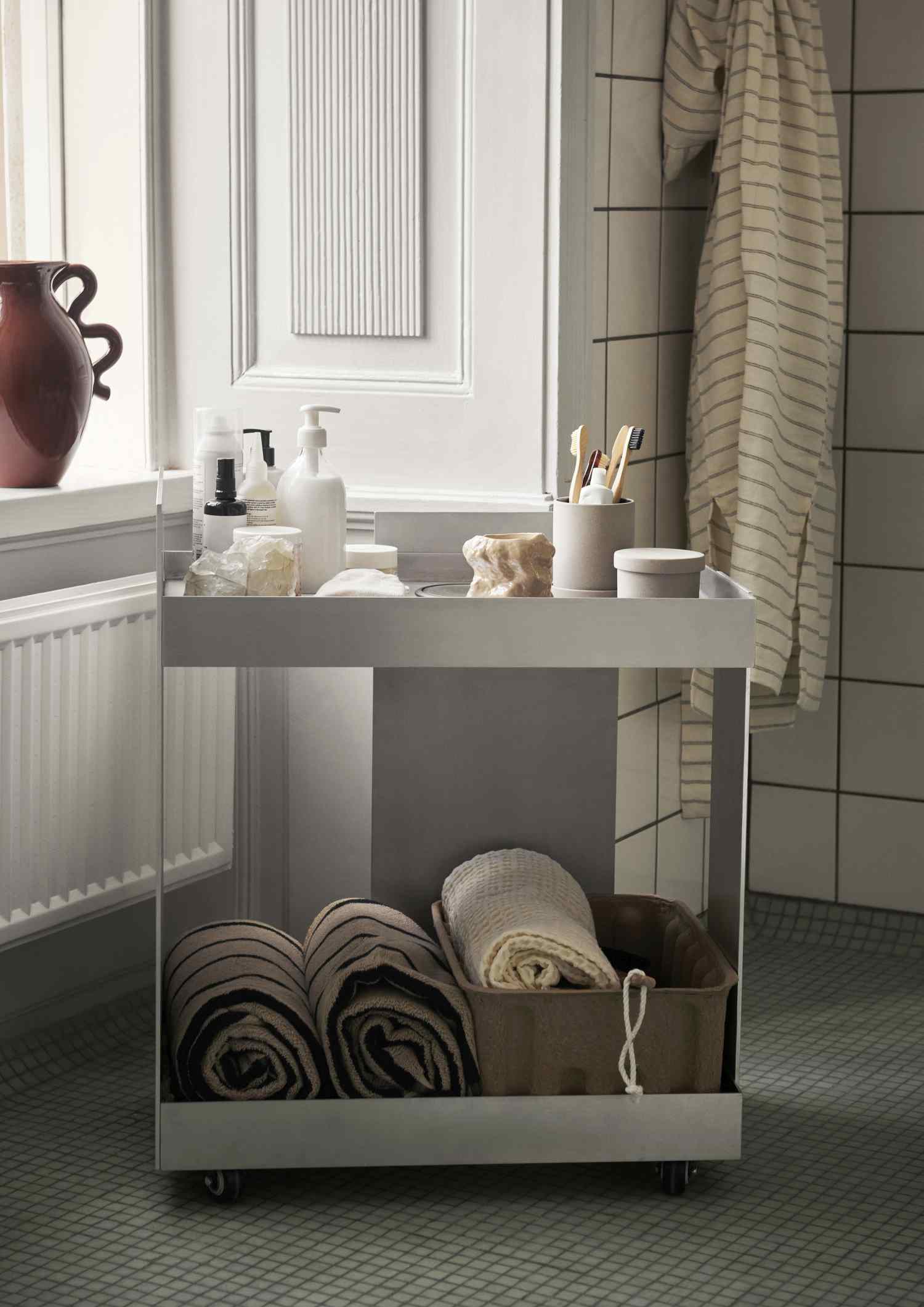 Ferm Living Servierwagen aus Aluminium im Badezimmer mit Handtüchern und Pflegeprodukten.