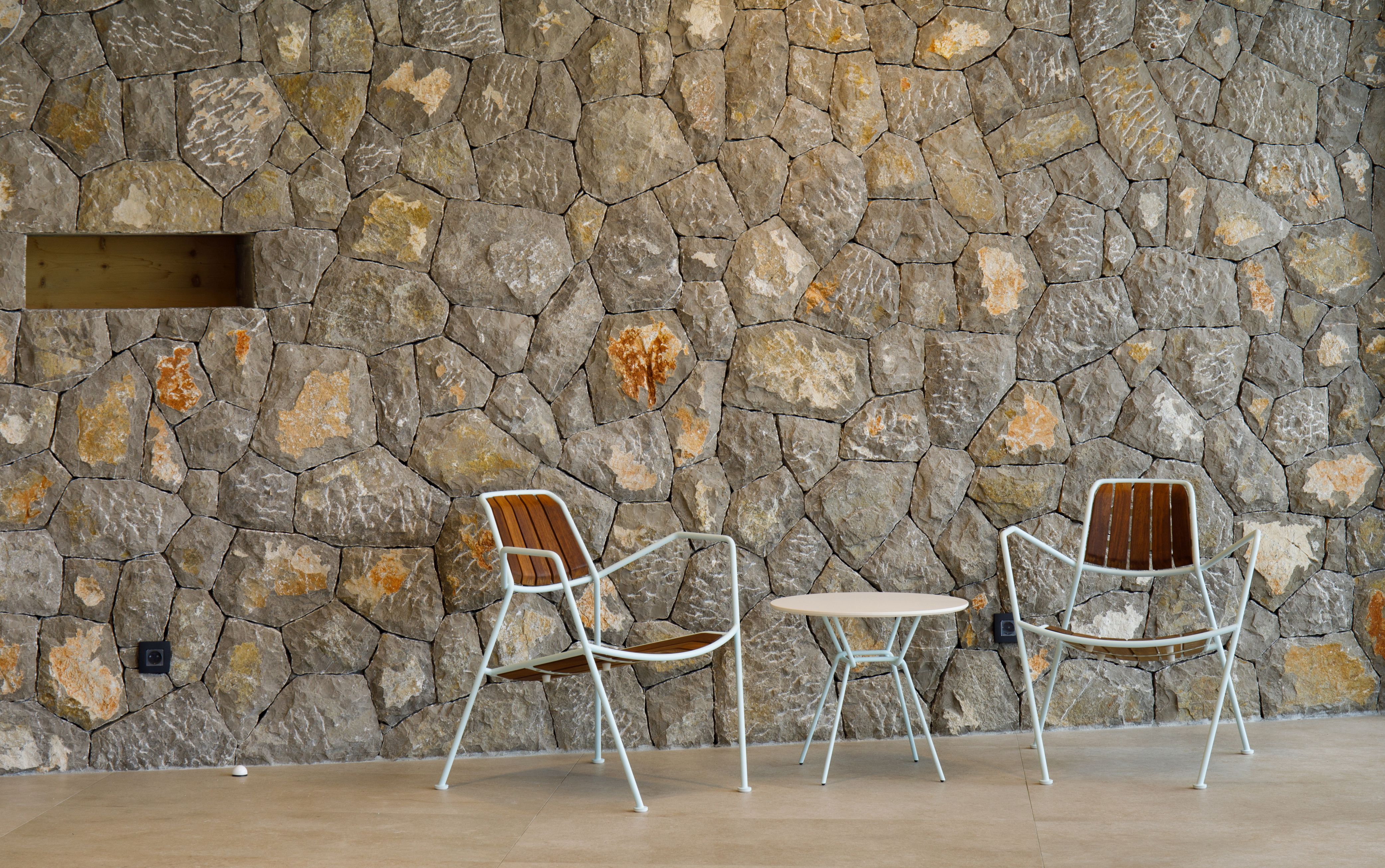 Zwei Osmo Outdoor Teak Stühle von Prostoria und ein Tisch vor einer Steinwand.