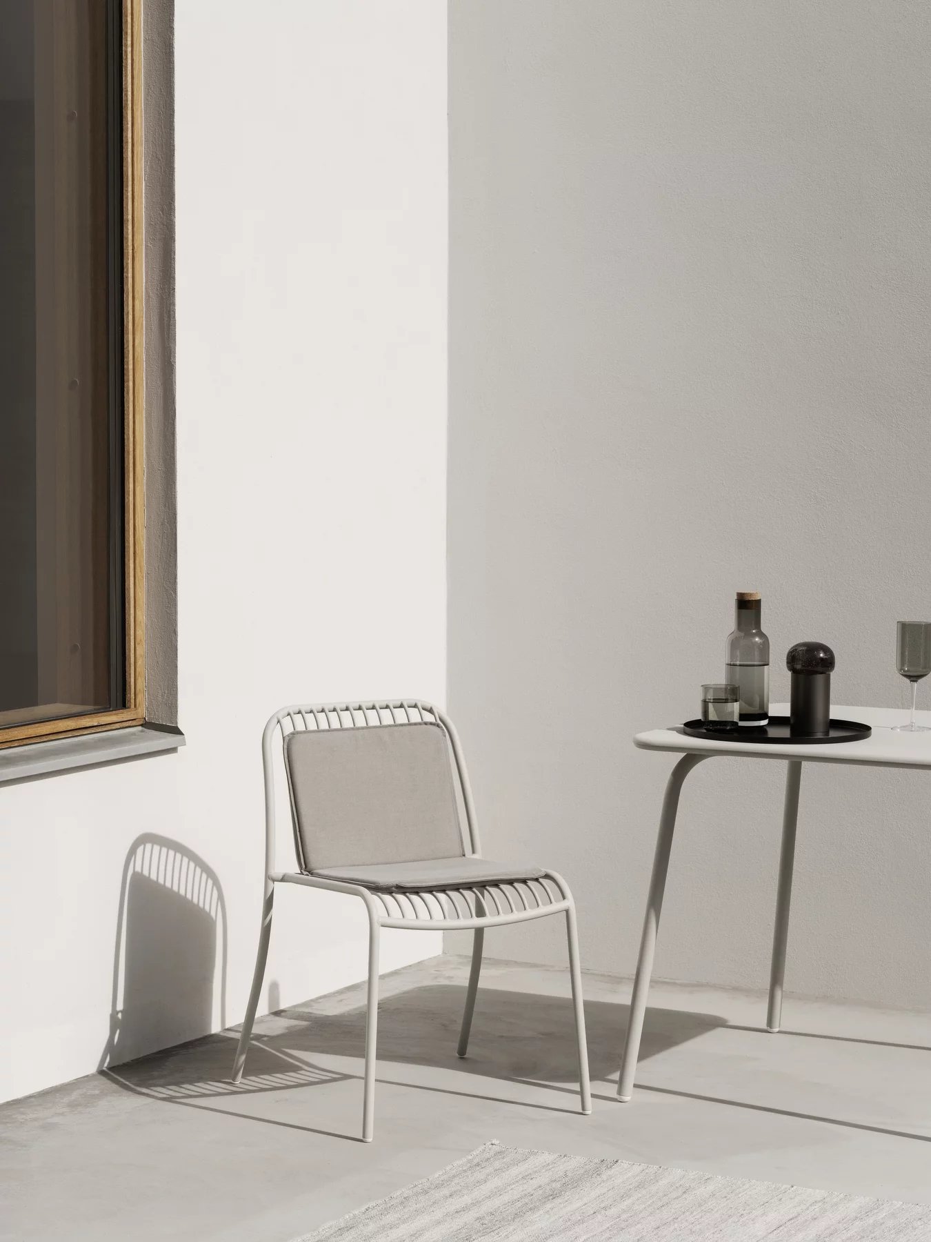 Blomus Yua Wire Chair Outdoor: Moderner, weißer Metallstuhl mit grauen Kissen auf Terrasse.