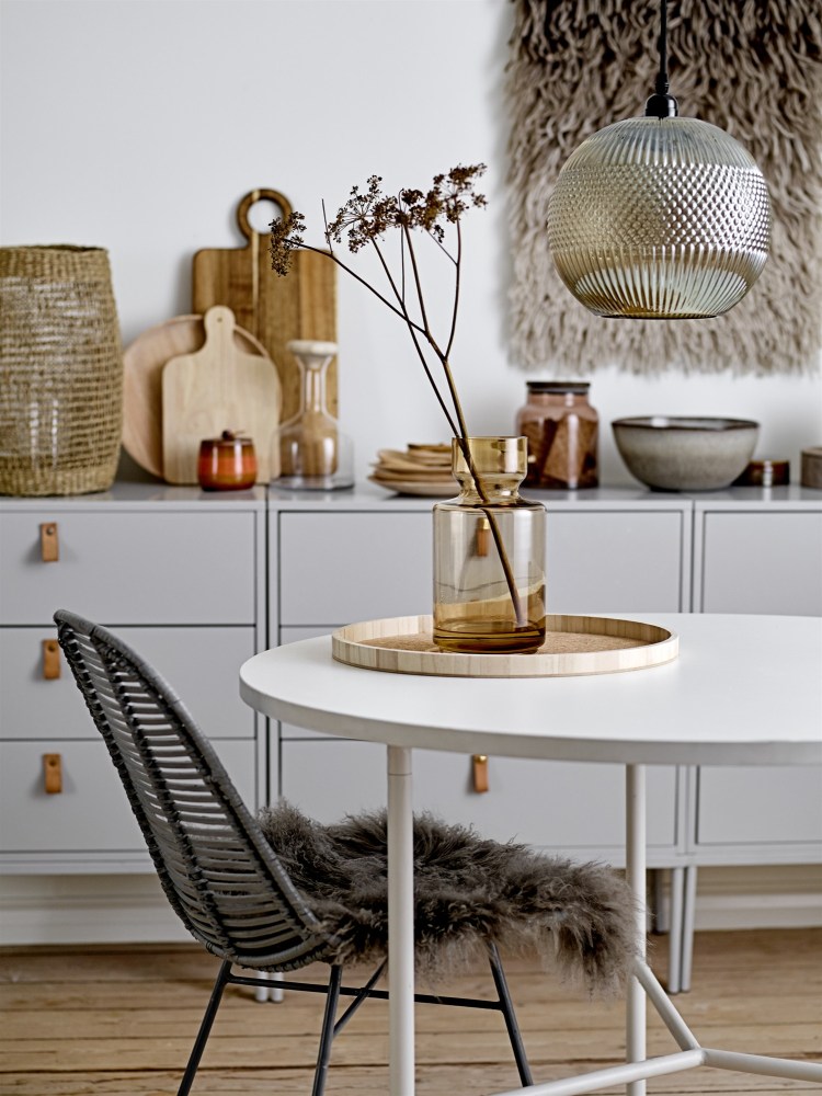 Esszimmer Interieur mit weißem Esstisch, Rattanstuhl mit Fell, Glasvase und moderner Pendelleuchte.