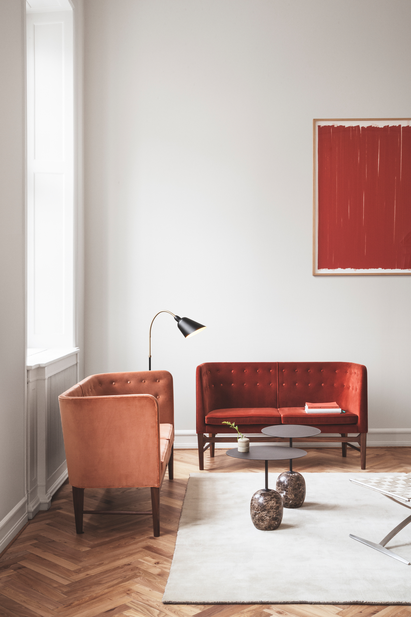 Einrichtungsbeispiel mit warm-schwarzem, ovalem Lato Beistelltisch von AndTradition, rotem Sofa und Sessel auf einem hellen Teppich.