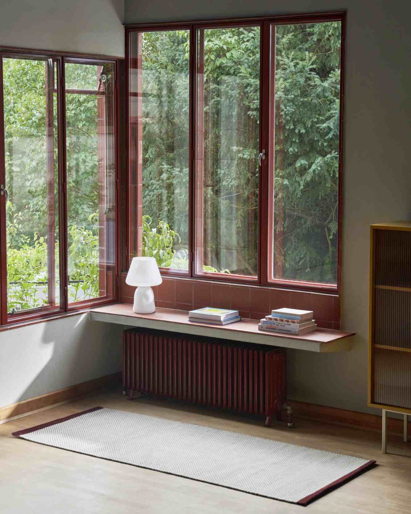 Heller Bias Rug Tint Teppich von Hay im Raum mit großem Fenster und Heizkörper.