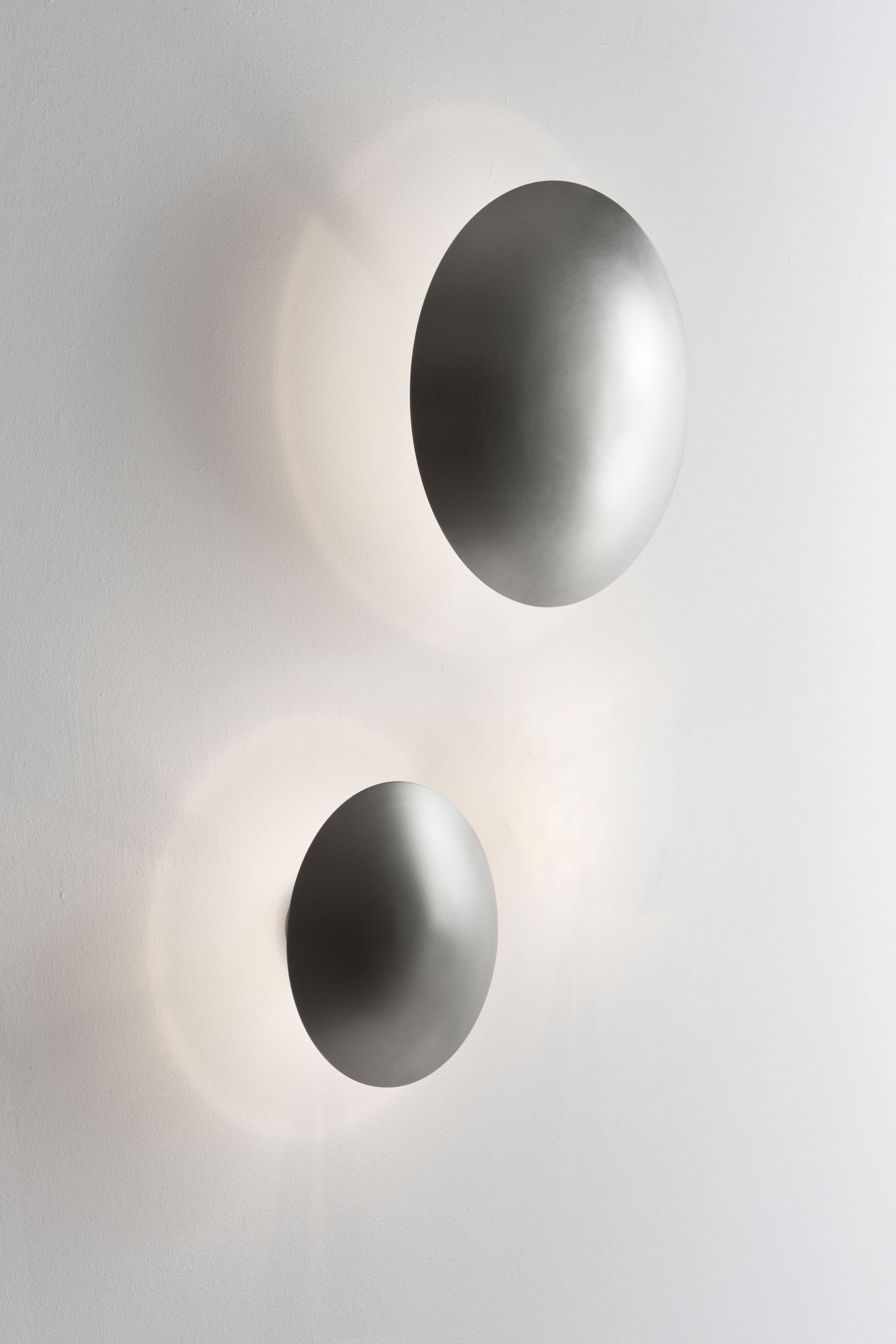 Zwei silberne Disco Wandleuchten von Santa & Cole an einer weißen Wand.