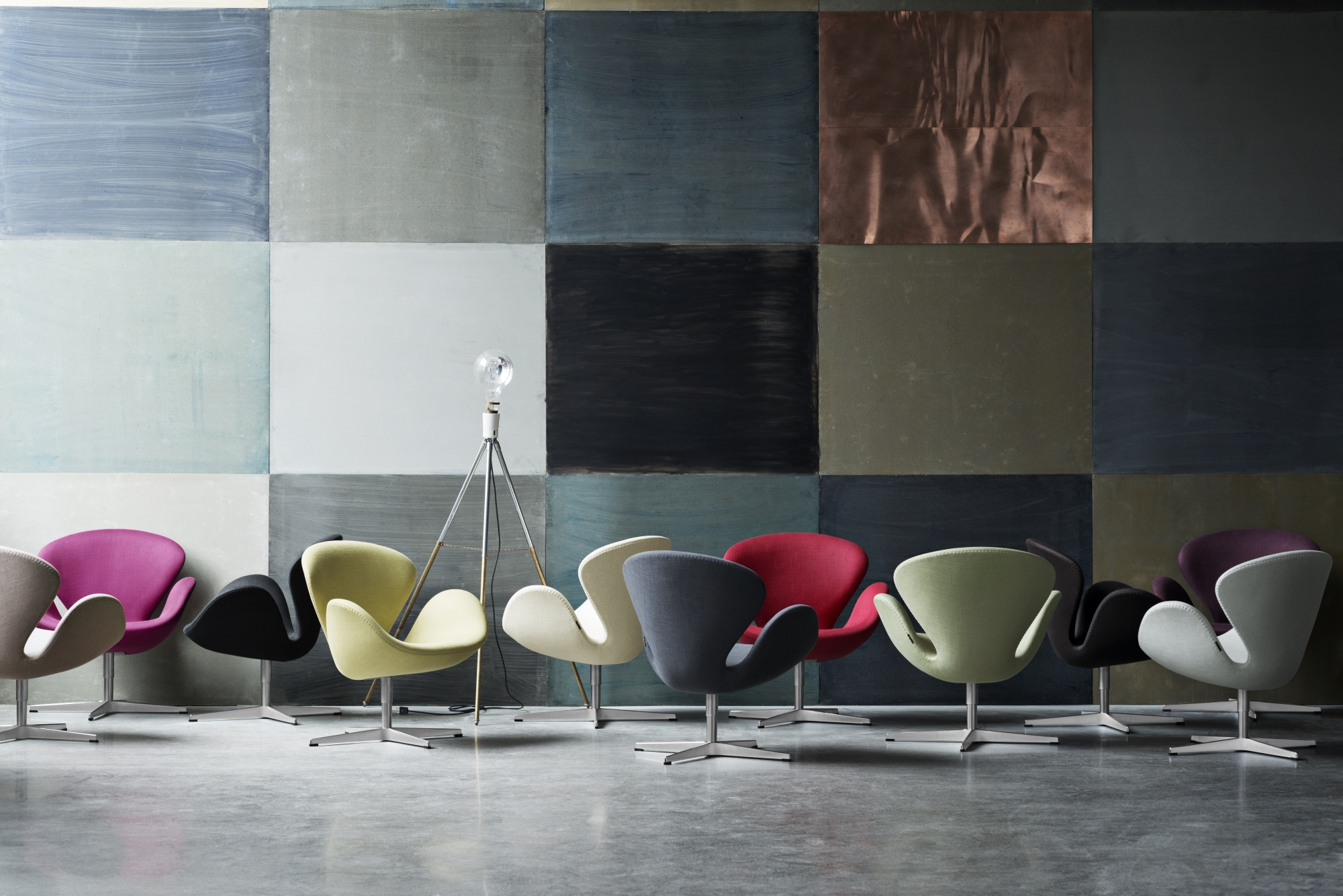 Fritz Hansen Schwan Sessel in verschiedenen Farben vor einer Wand mit Farbquadraten.