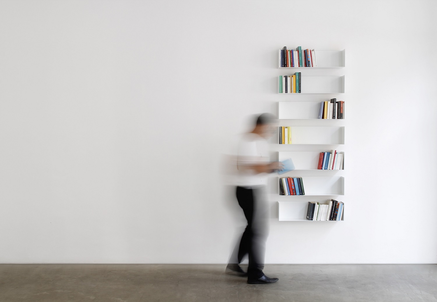 Weißes Taschenbuchregal a Linea1 von Müller Möbelwerkstätten an einer Wand mit Büchern und Person.