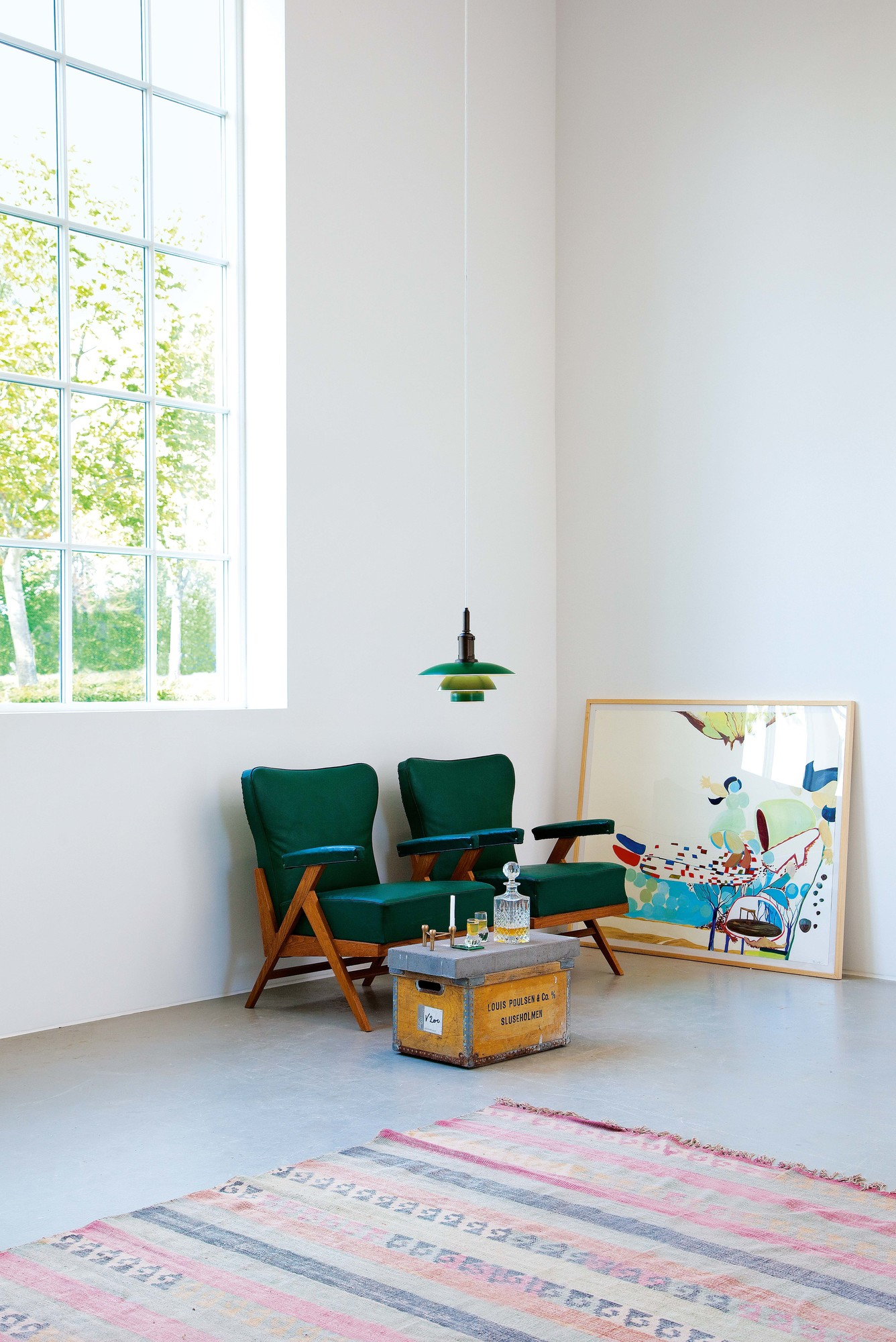 Moderne grüne PH Louis Poulsen Hängeleuchte über zwei grünen Sesseln in einem hellen Wohnzimmer.