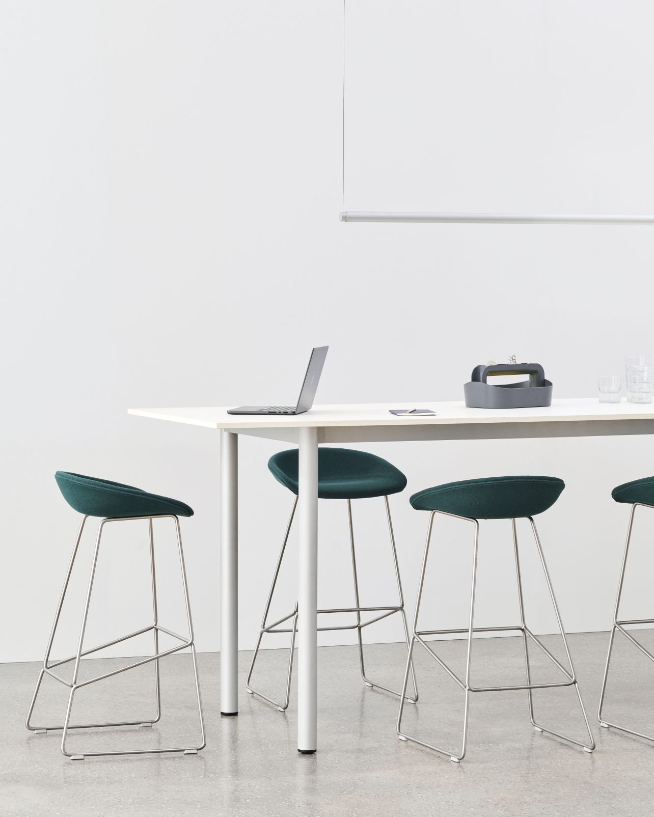Annex Table Overhang Esstisch von Hay mit Laptop und grünen Hockern in minimalistischem Büro.