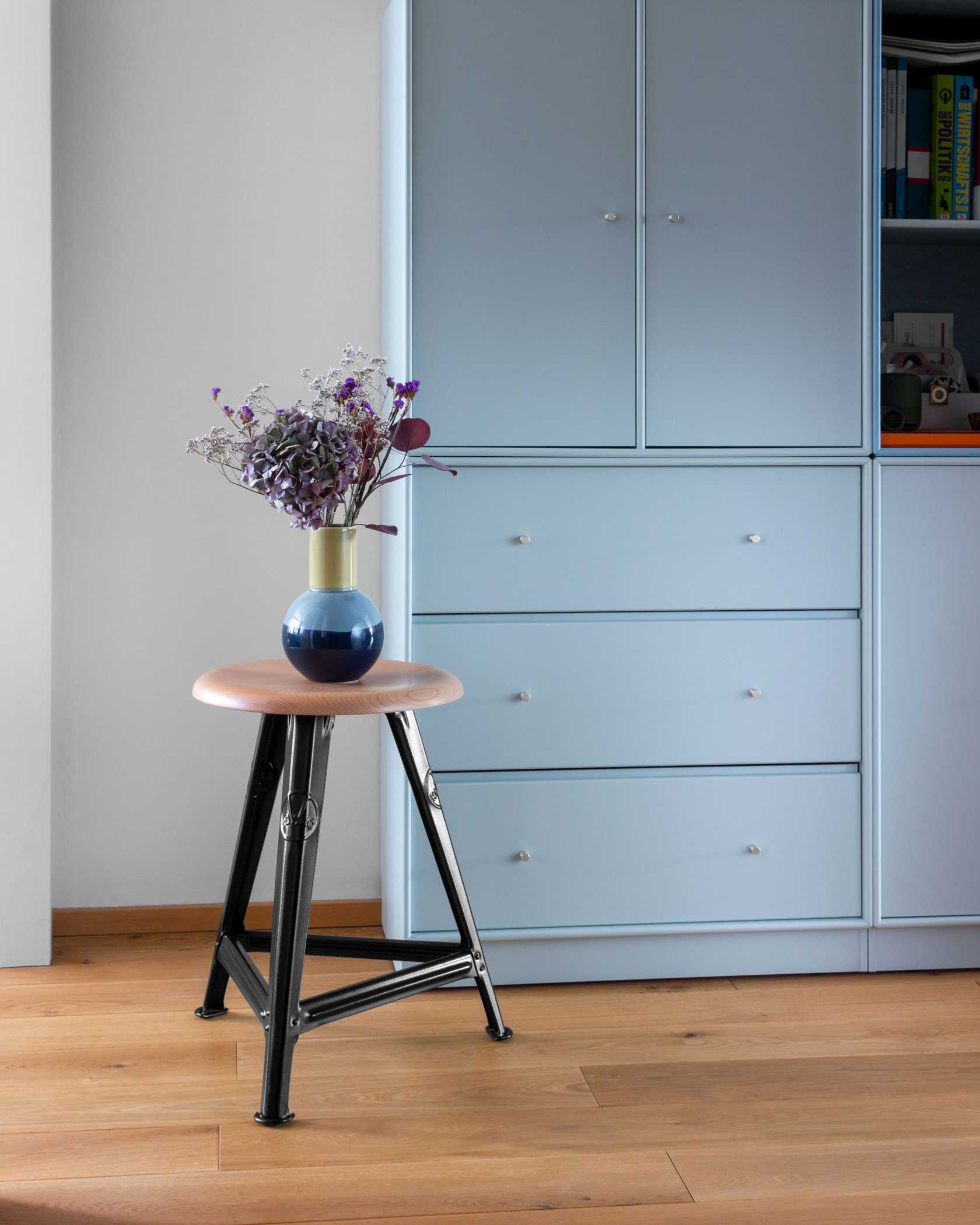 Rowac Schemel Model I 50 cm Hocker mit Holzsitz und schwarzem Metallgestell, Vase mit Blumen.