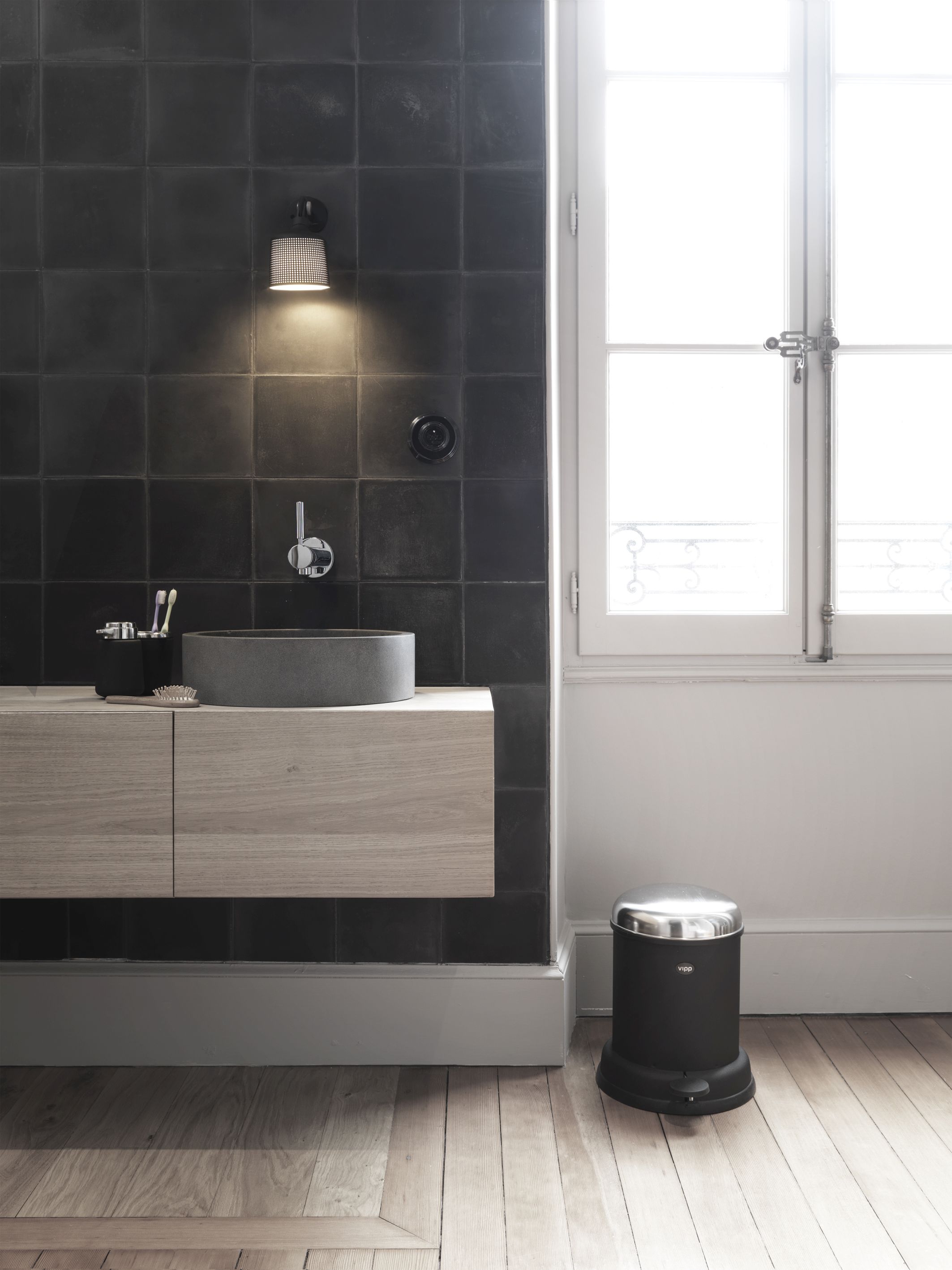 Schwarzer Vipp Treteimer 4 Liter im modernen Badezimmer mit Holzfußboden und schwarzen Fliesen. Design Mülleimer für Bad.