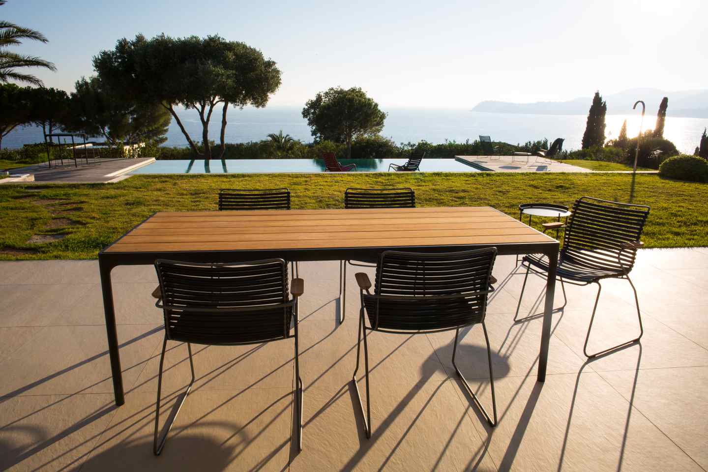 Houe Four Esstisch Outdoor mit Stühlen auf Terrasse mit Pool und Meerblick.