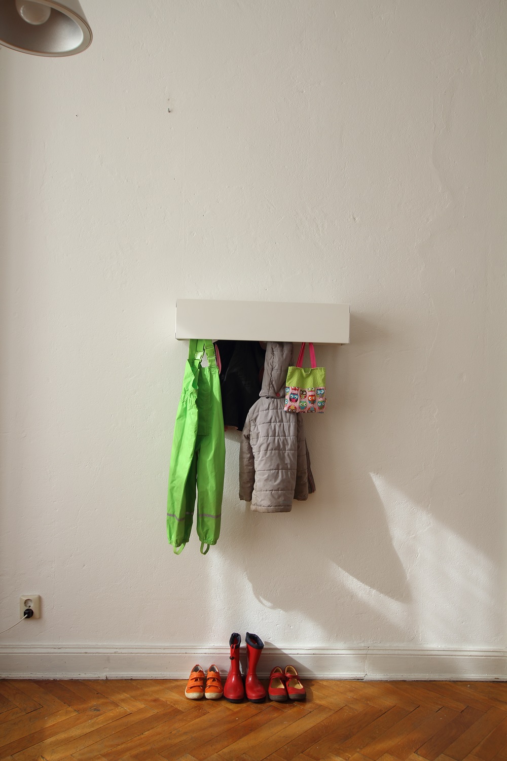 Weiße Wandgarderobe CR Linea1 von Müller Möbelwerkstätten mit Kinderkleidung und Schuhen an einer weißen Wand.