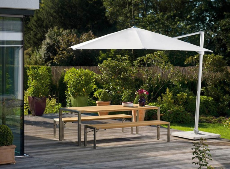 Weißer Ampelschirm über Gartentisch mit Bänken auf Holzterrasse, ideal für entspannte Stunden im Freien.