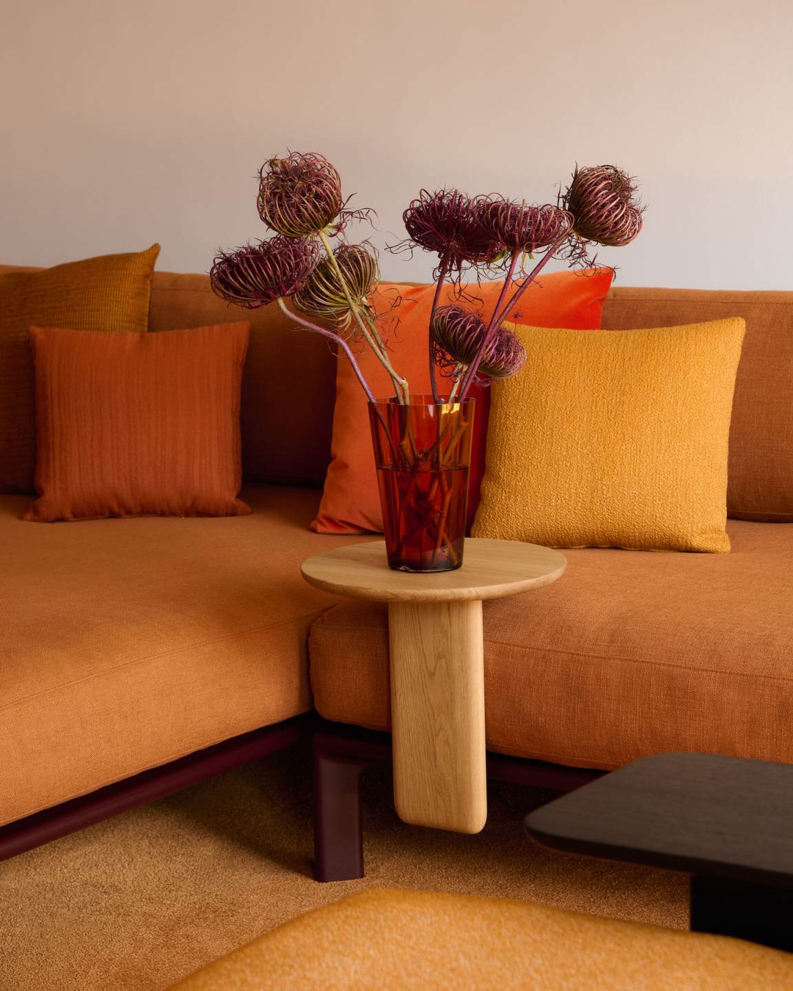 Nahaufnahme des Vitra Anagram Anstecktisches mit Blumen auf einem orangefarbenen Sofa, modernes Wohnzimmerdesign.