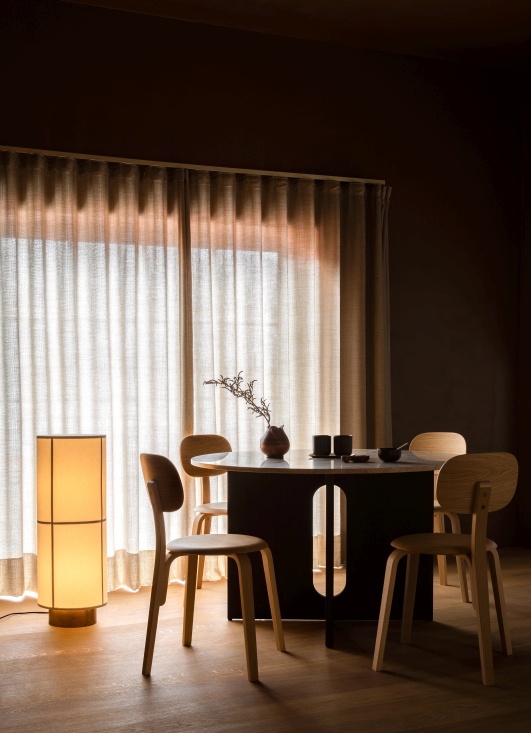 Audo Hashira Stehleuchte im Interieur neben Esstisch und Stühlen, warmes Licht, gemütliche Atmosphäre.