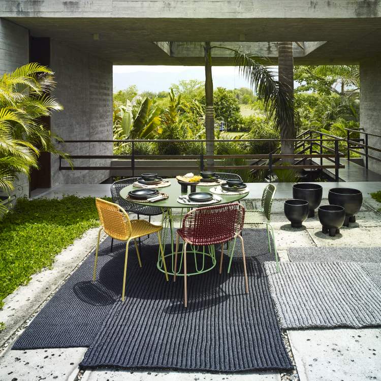 Outdoor-Essbereich mit rundem Tisch, bunten Stühlen und modernen Teppichen für Terrasse und Garten.