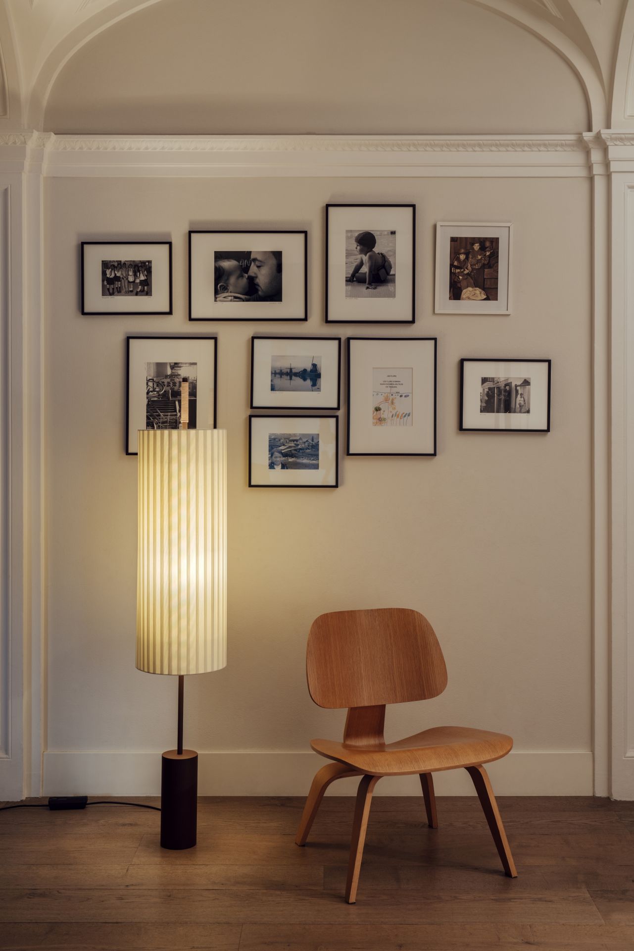 Stehleuchte mit Stoffschirm und Holzstuhl vor Bilderwand im Wohnzimmer. Moderne Innenarchitektur.