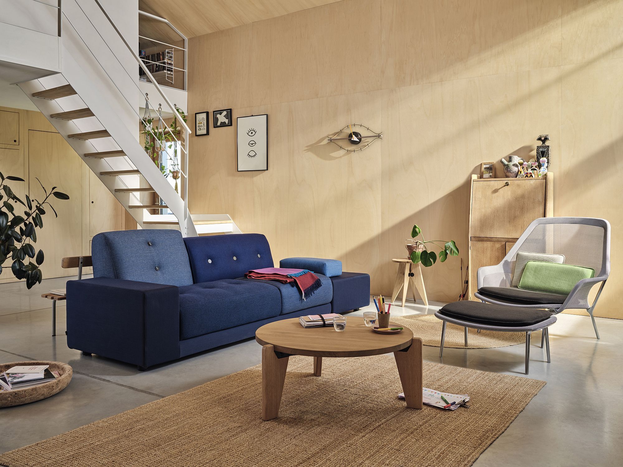 Helles Wohnzimmer mit blauem Sofa, Holztisch und einem Vitra Slow Chair Sessel mit Fußhocker.