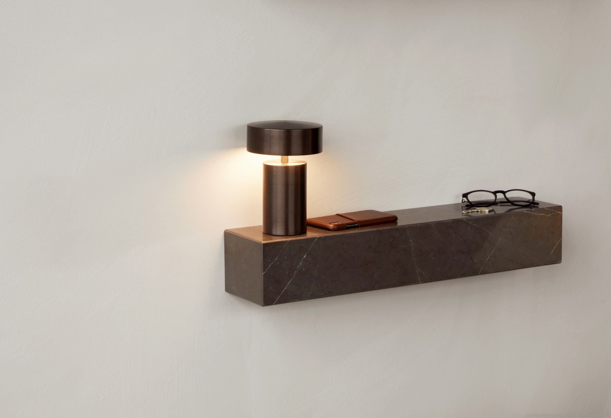 Audo Copenhagen Plinth Shelf Regal aus Marmor mit Lampe, Handy, Brille und Schlüssel an der Wand.