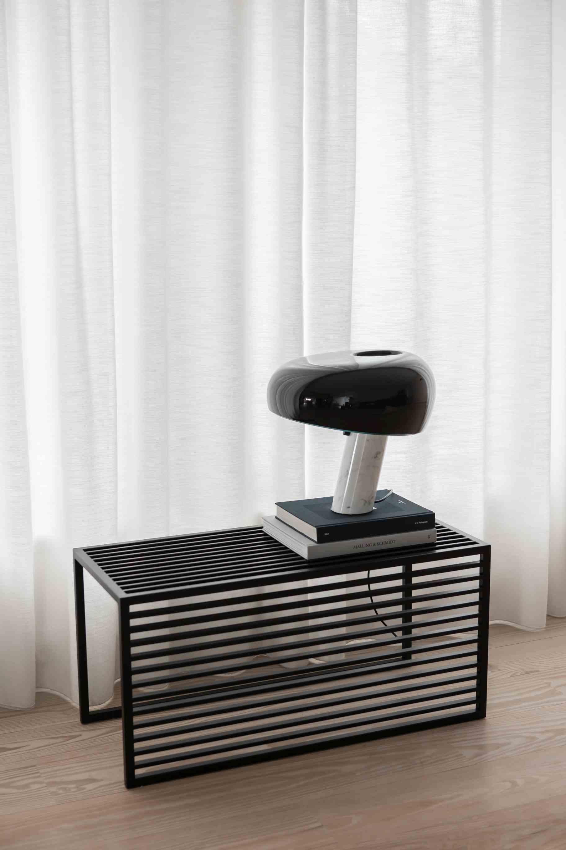 Schwarze Element Bench Bank von Novoform mit Lampe und Büchern vor weißem Vorhang.