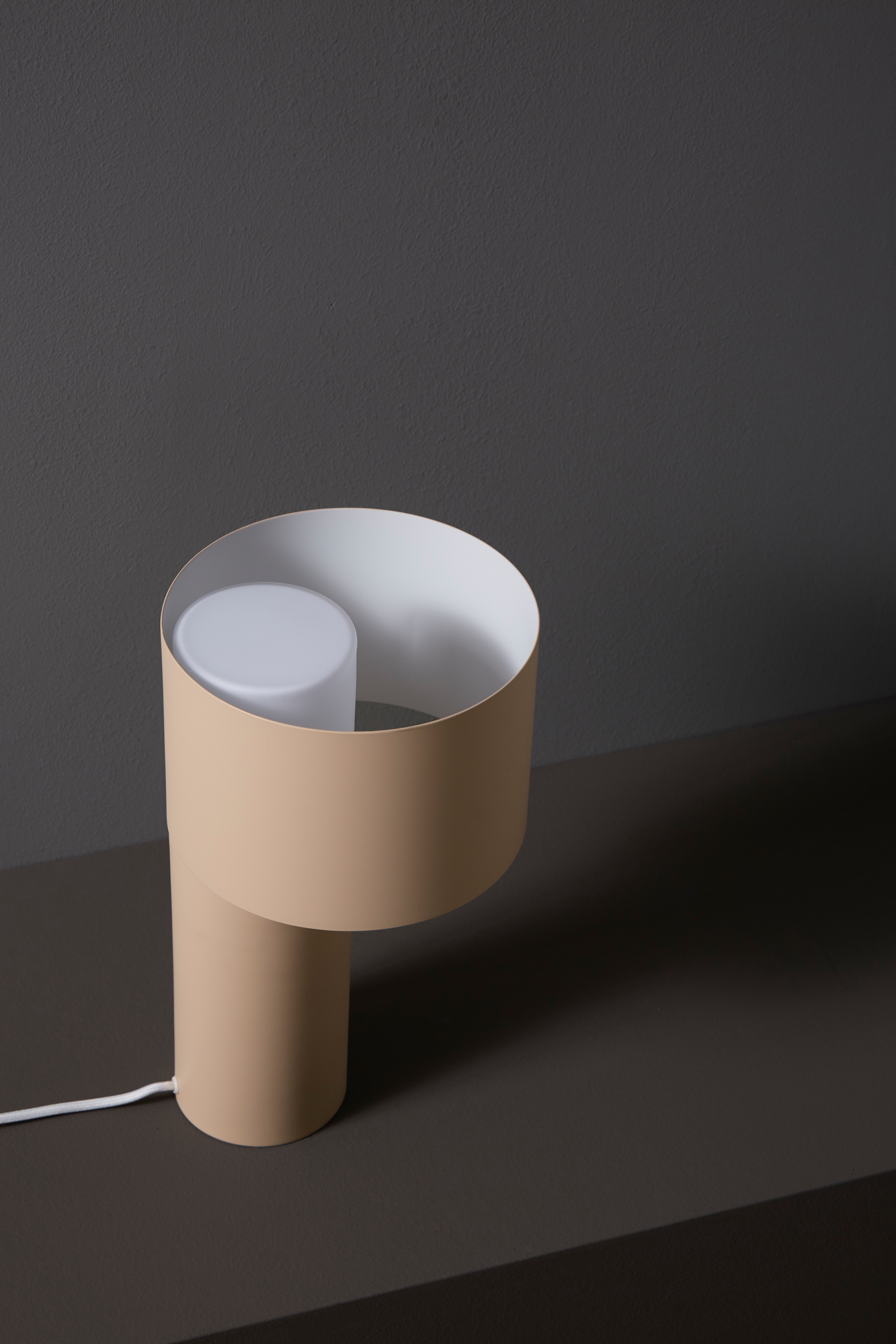 Beige Tangent Tischleuchte von Woud auf dunklem Untergrund, modernes Design mit zylindrischem Lampenschirm und weißem Innenleben.