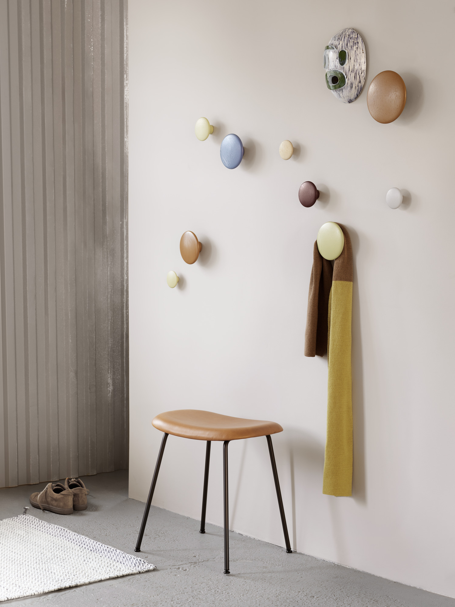 Muuto Fiber Stool Hocker mit brauner Sitzfläche und schwarzen Beinen vor einer Wand mit Garderobenhaken.